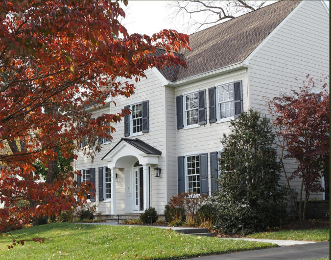 Garden District Napanee Elegant brick townhouse entrance with arched windows, ornate stonework, and a wooden front door accessed by a black metal staircase. Vibrant flower arrangements in planters and hanging baskets add color, while a red brick pathway and lush greenery create a
